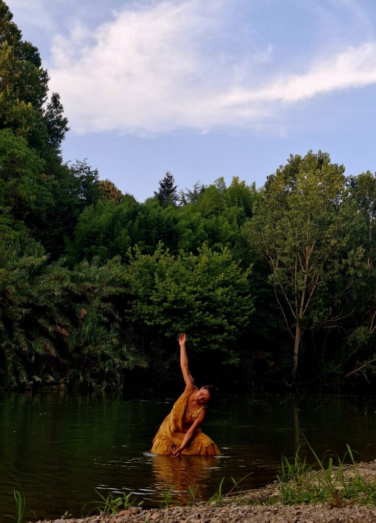Una danzatrice in abito giallo nel Tevere, un braccio teso verso il cielo, per Scultura Corale 01 di Alessandro Piergallini